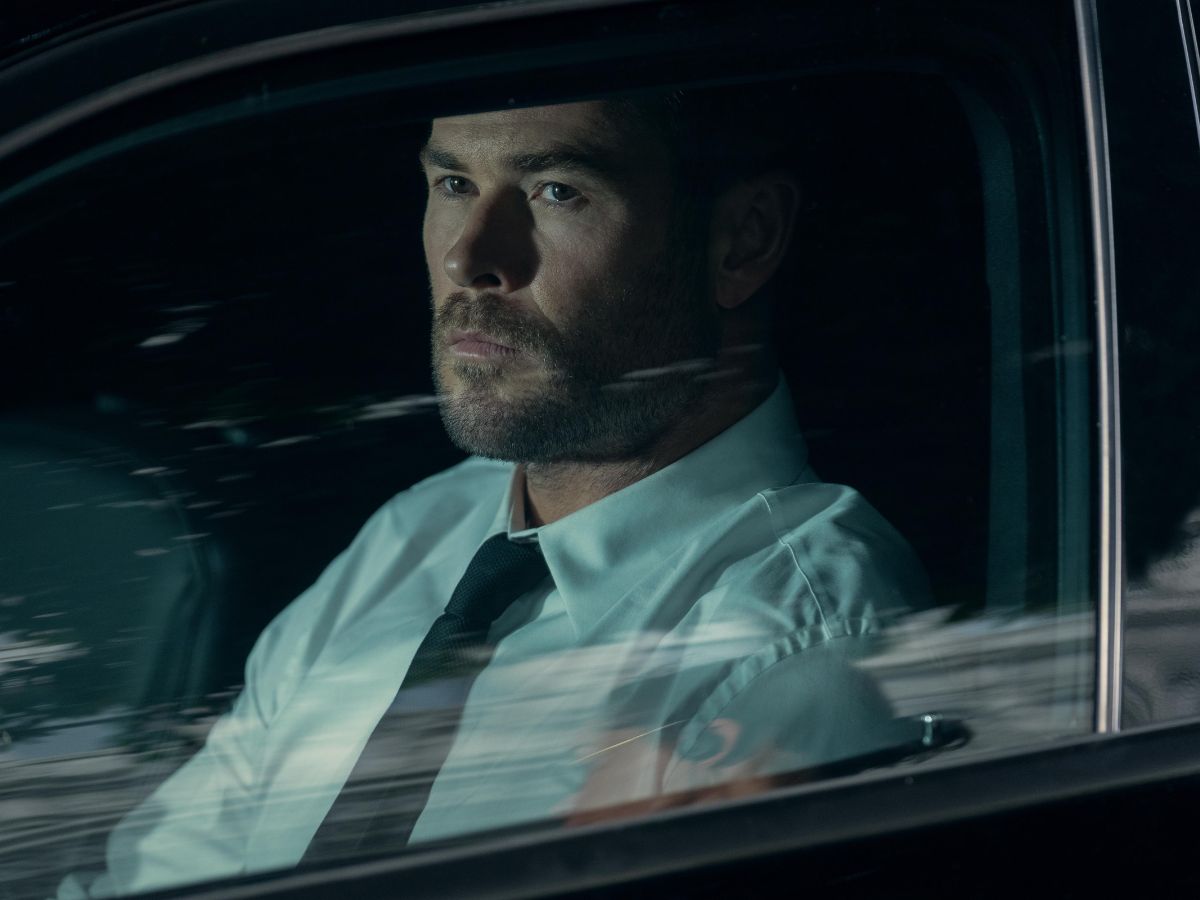 Chris Hemsworth en un coche con camisa blanca y corbata negra en una secuencia de su película "Ruta de escape"