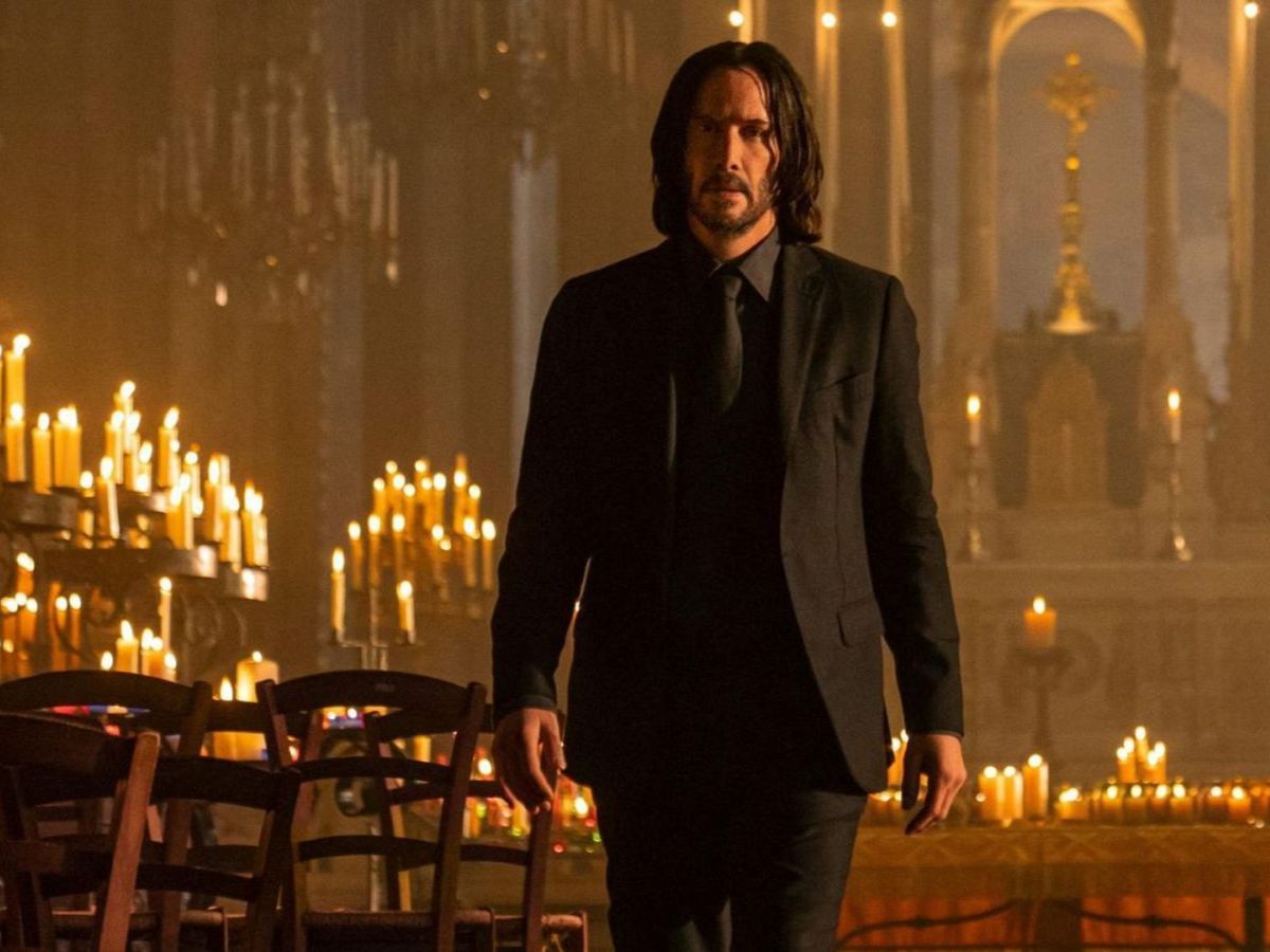 Keanu Reeves vestido con chaqueta y pantalón negro en una iglesia llena de velas en John Wick 4.