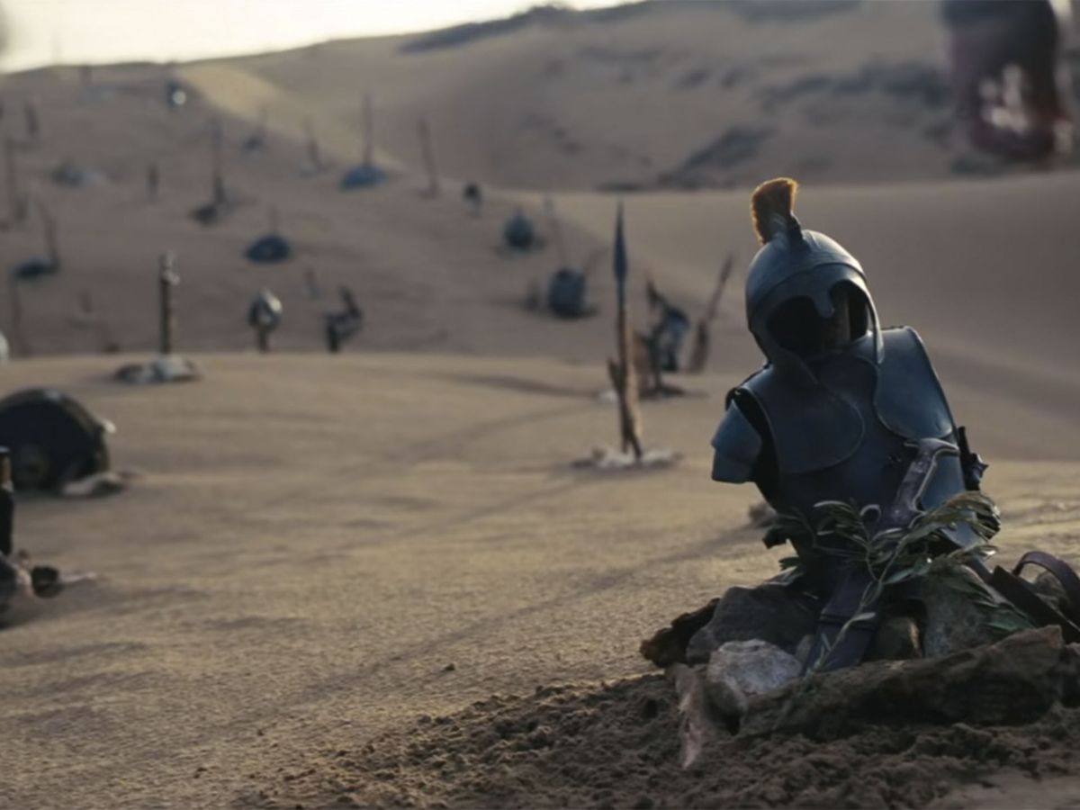 Cascos de soldados y trajes en la arena tras la guerra de Troya en La Odisea de Christopher Nolan.