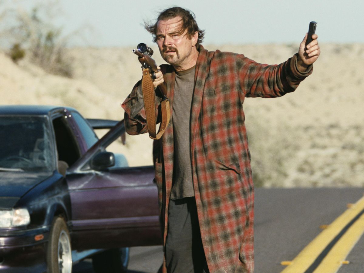 Leonardo DiCaprio con una chaqueta de cuadros rojos y una pistola en la mano en una escena de la película Una batalla tras otra.