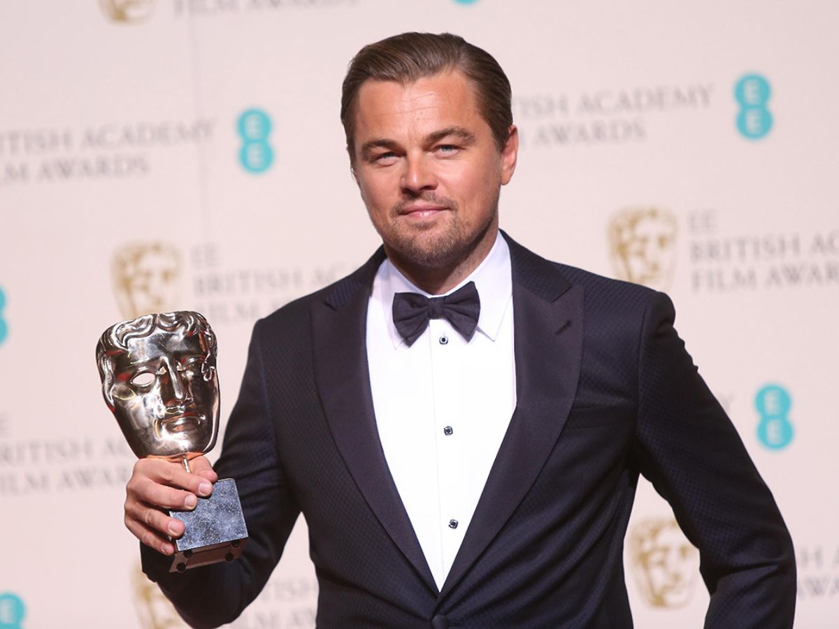Leonardo DiCaprio con traje de chaqueta negra, camisa blanca y pajarita negra sujetando su Premio BAFTA.