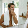 hombre muy atractivo, como de 40 años, poniéndose crema en el rostro después de darse un baño