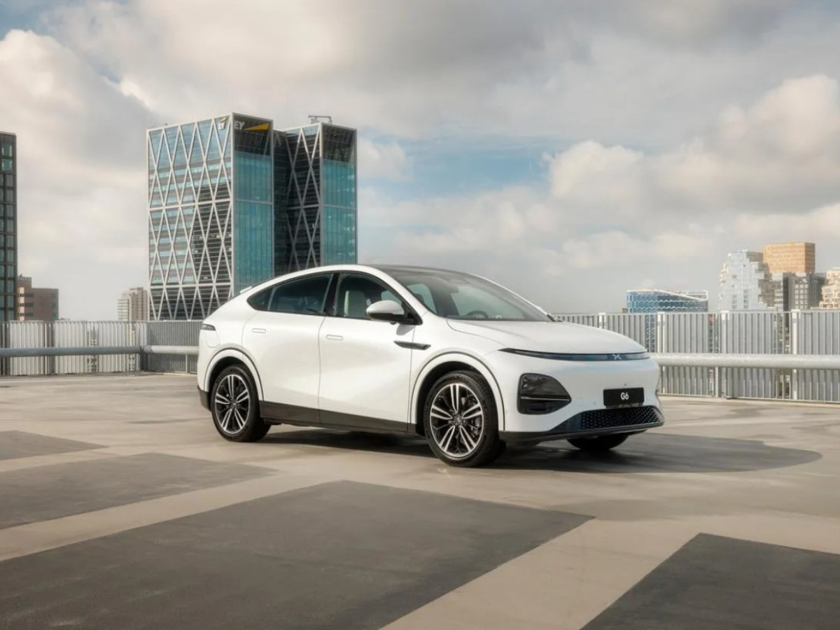 XPeng G6 blanco aparcado en una carretera con un edificio de cristal de fondo