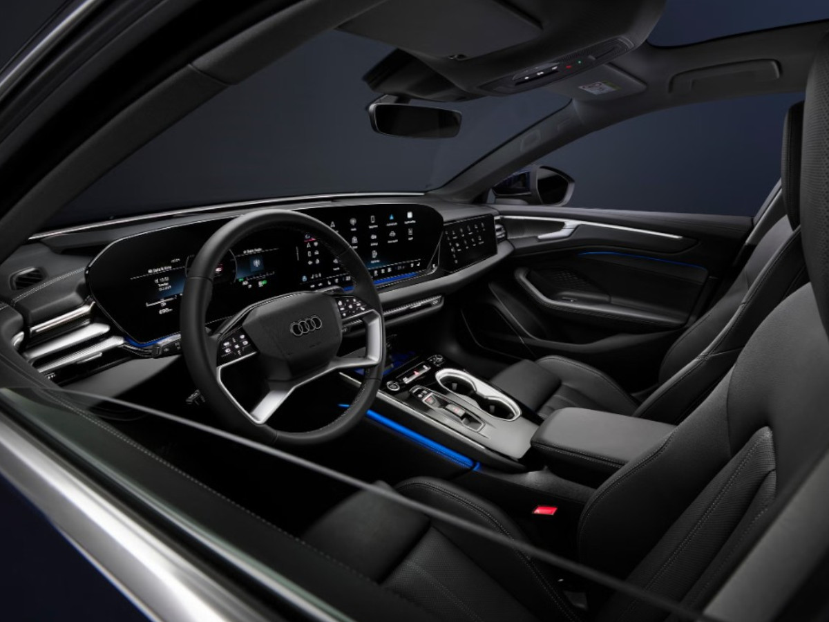 Interior del Audi A6 con volante a la izquierda, salpicadero en color negro, doble pantalla central táctil, instrumentación digital y asientos delanteros tapizados en cuero oscuro.