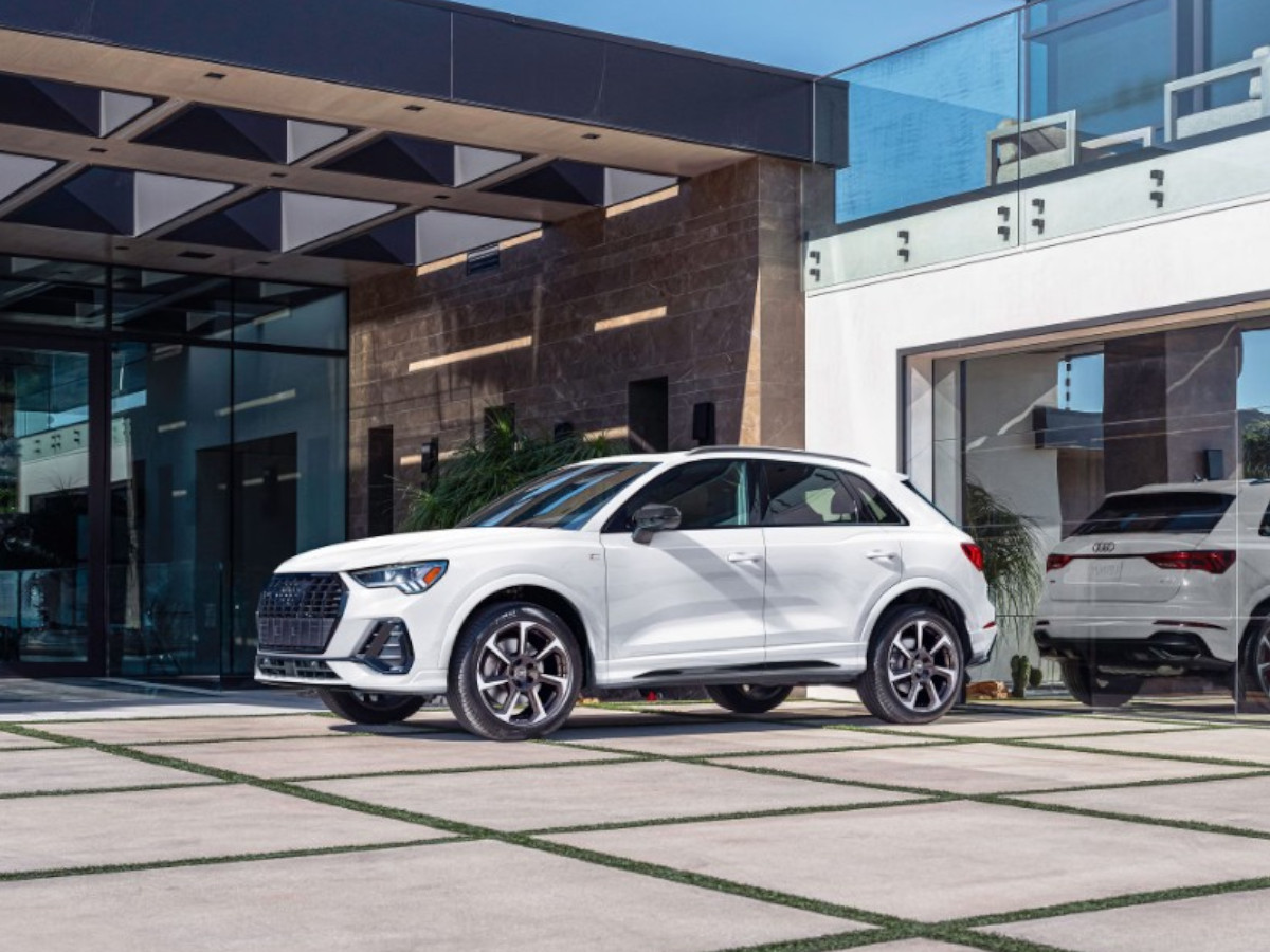 SUV compacto Audi Q3 de color blanco, aparcado frente a una vivienda moderna, visto desde el lateral y el frontal, con carrocería elevada y llantas de gran tamaño.