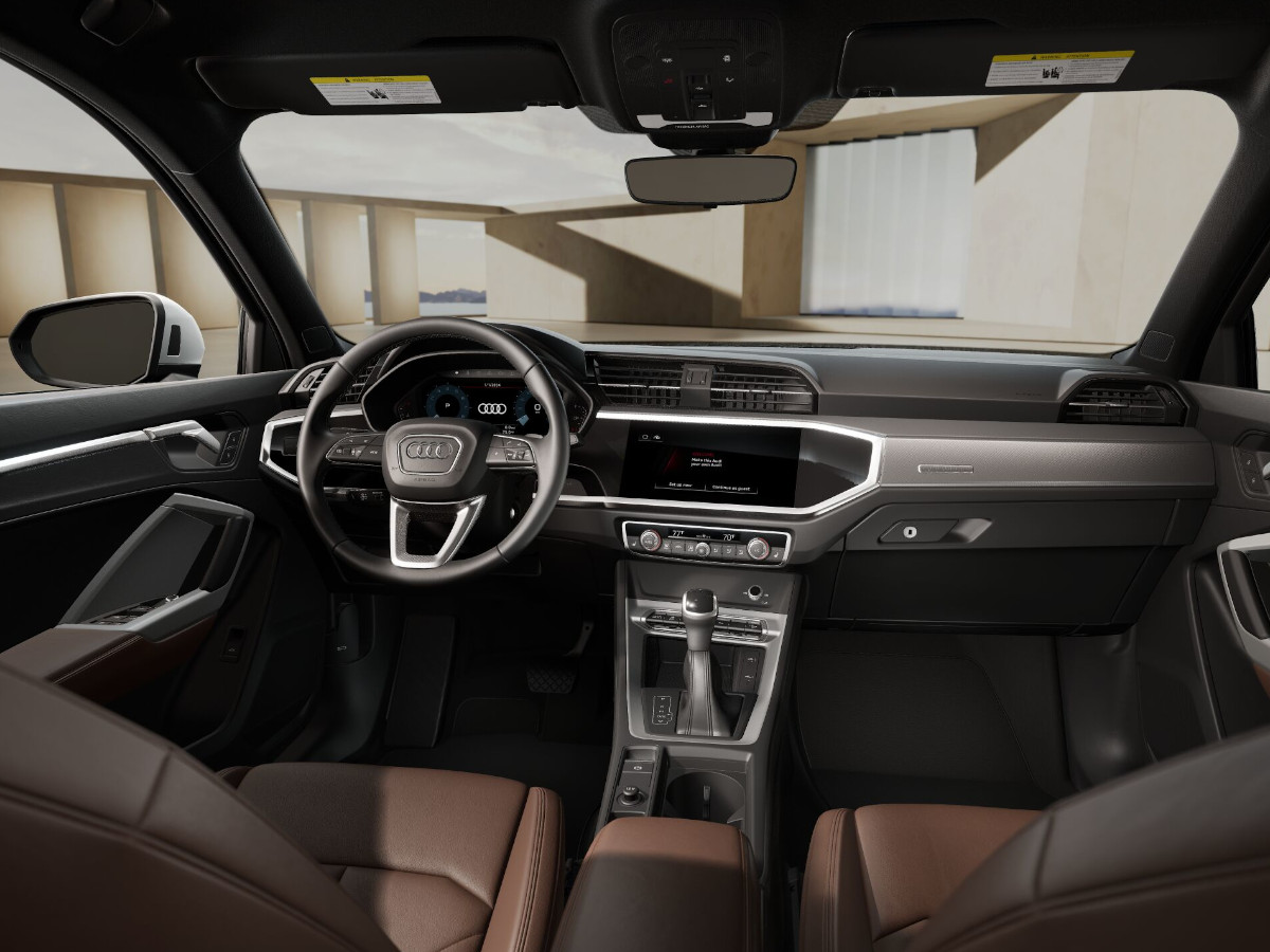 Interior del Audi Q3 con volante a la izquierda, salpicadero en tonos oscuros, instrumentación digital Audi Virtual Cockpit, pantalla central integrada y asientos delanteros tapizados en cuero marrón.