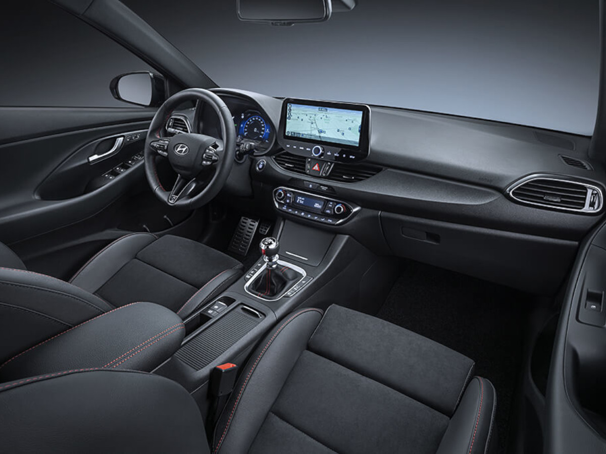Interior del Hyundai i30 con volante a la izquierda, salpicadero en color negro, cuadro de instrumentos digital, pantalla central táctil con navegación y asientos delanteros tapizados en tela oscura.