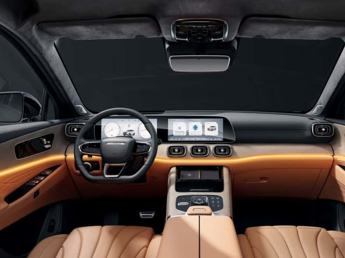 Interior del SUV Jaecoo 8 con volante a la izquierda, salpicadero en tonos negros y marrones, doble pantalla digital integrada en el tablero y asientos tapizados en cuero claro con costuras visibles.