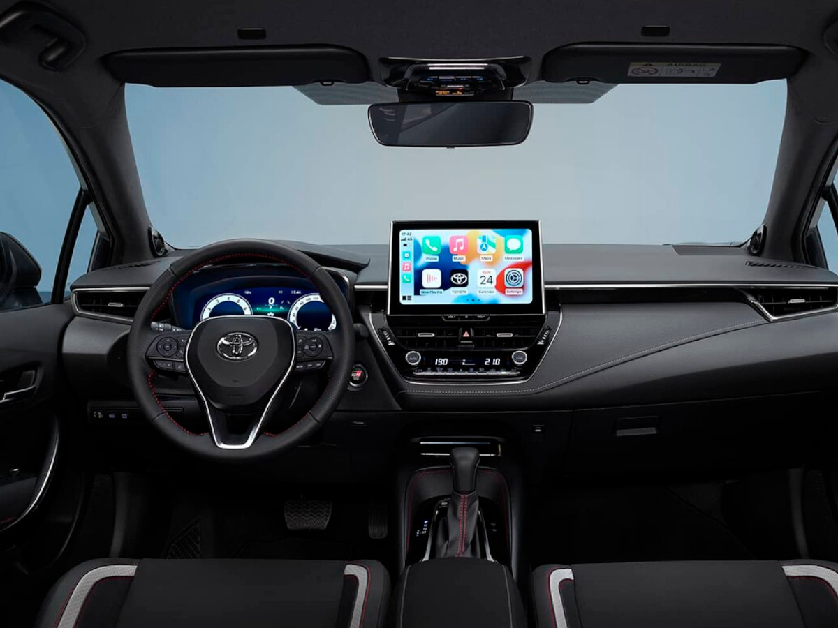 Interior del Toyota Corolla híbrido 2.0 con volante a la izquierda, salpicadero en color negro, cuadro de instrumentos digital y pantalla central táctil encendida con el sistema multimedia