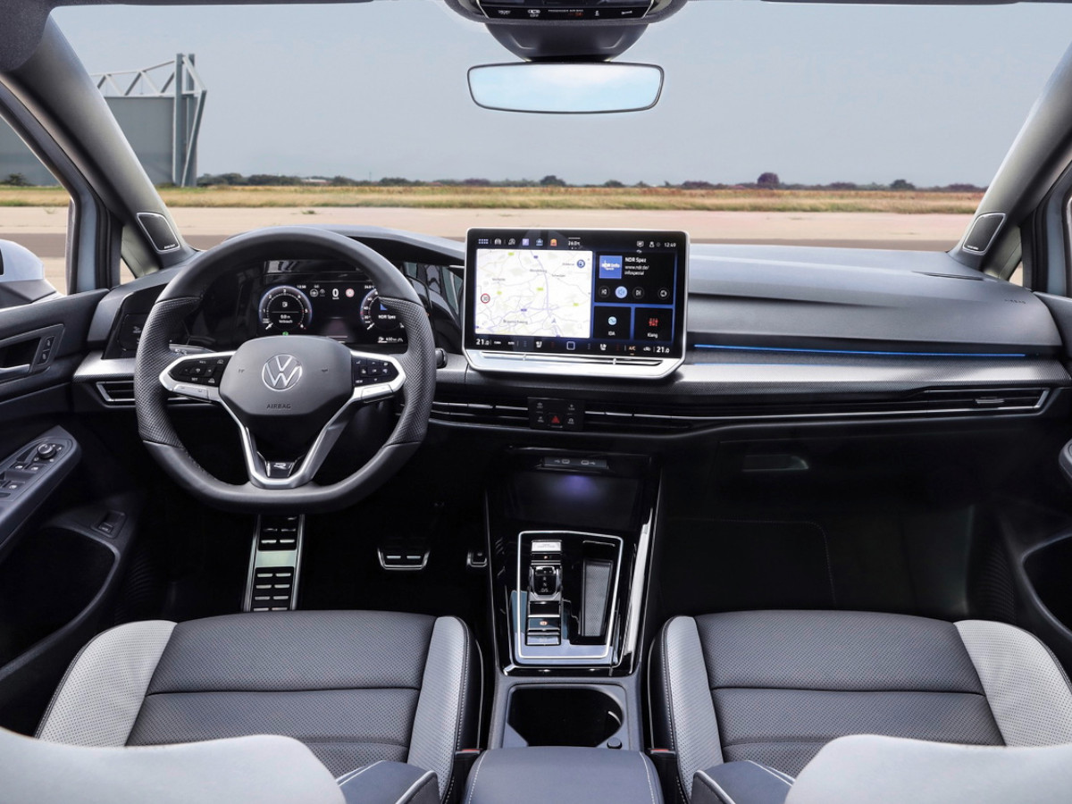 Interior del Volkswagen Golf con volante a la izquierda, salpicadero en color oscuro, cuadro de instrumentos digital y pantalla central táctil mostrando el sistema de navegación.