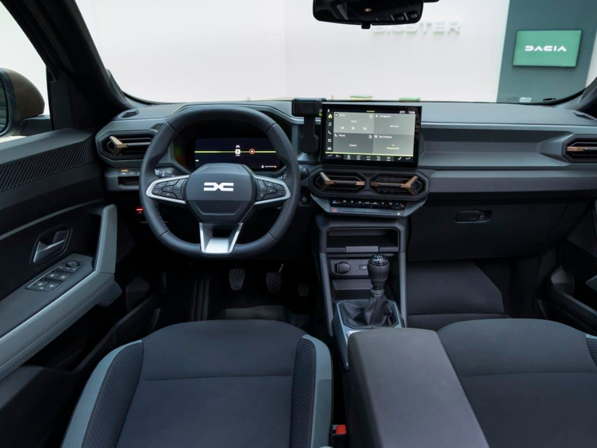 Interior del Dacia Bigster visto desde las plazas traseras, con salpicadero horizontal, pantalla central flotante, volante multifunción y asientos de tela en tonos oscuros.