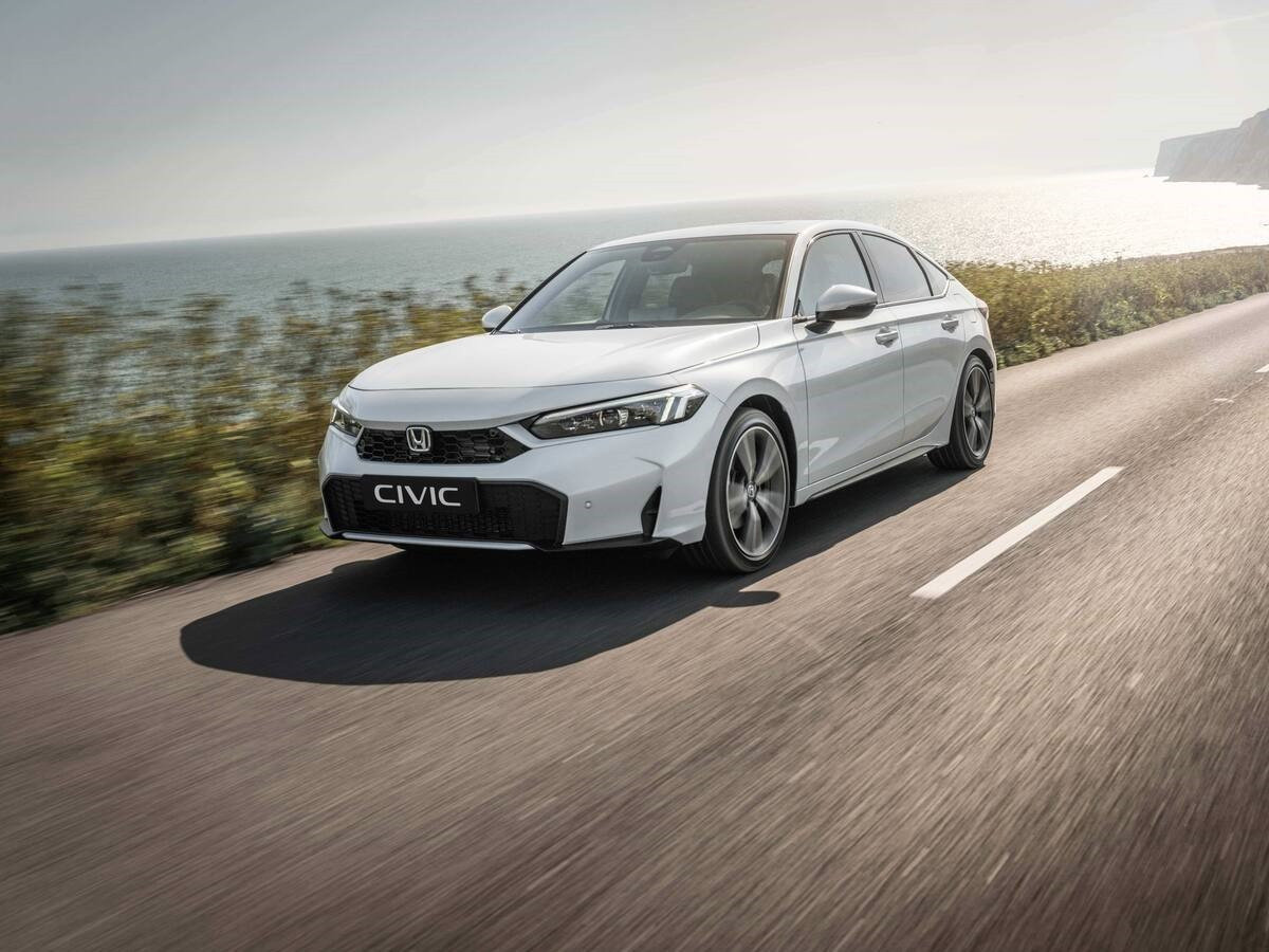 Honda Civic híbrido de color blanco circulando por una carretera costera, visto desde el frontal y lateral, con el mar y acantilados al fondo.