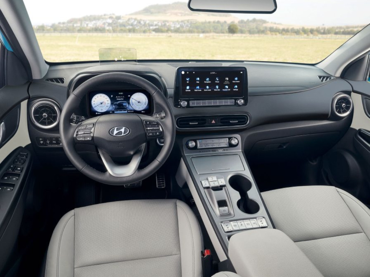Interior del Hyundai Kona Electric visto desde las plazas traseras, con volante multifunción, instrumentación digital, pantalla central táctil y consola elevada con selectores del cambio.