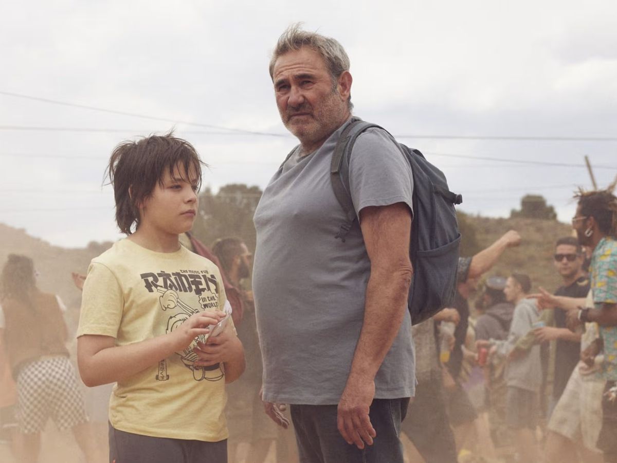 Bruno Núñez con una camiseta de manga corta amarilla y a su lado Sergi López con camiseta gris y mochila en una escena en el desierto en la película Sirat.