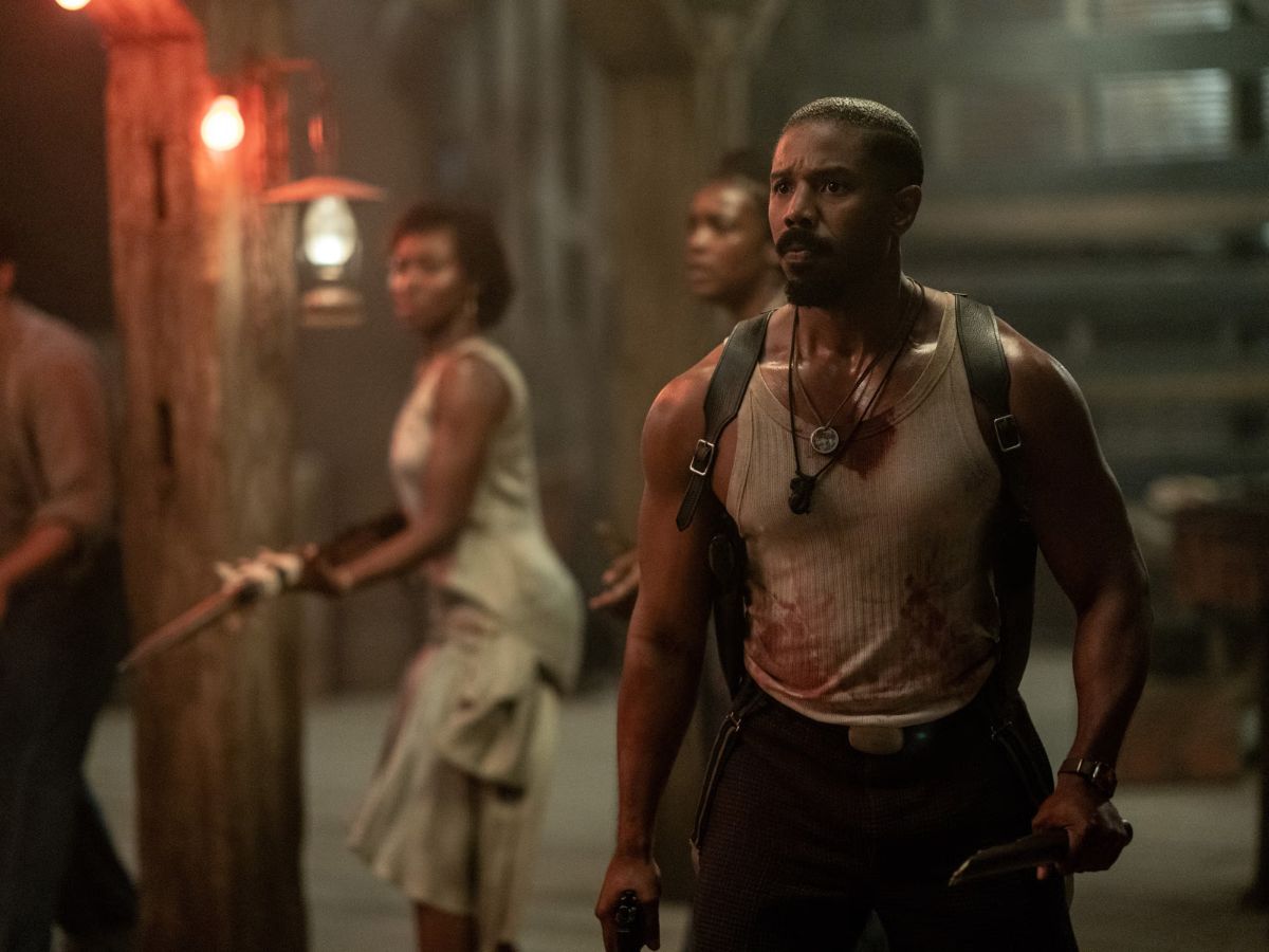 Michael B. Jordan con una camiseta de tirantes blanca y cubierto de sangre en una escena de la película Los pecadores.