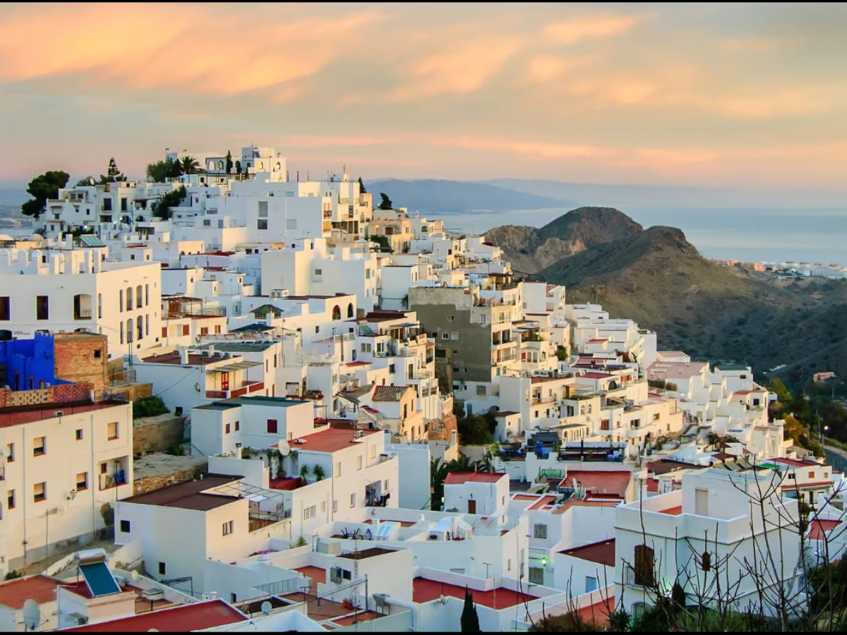 Vista panorámica de Mojácar, pueblo blanco de Almería, con casas encaladas escalonadas sobre una ladera, tejados planos y montañas al fondo al atardecer.