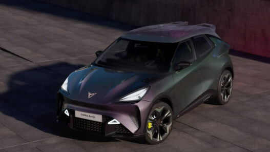 Coche eléctrico CUPRA Raval visto desde un ángulo frontal elevado, con carrocería en tonos verdes y morados, llantas deportivas y firma lumínica LED, estacionado en una plaza urbana de cemento