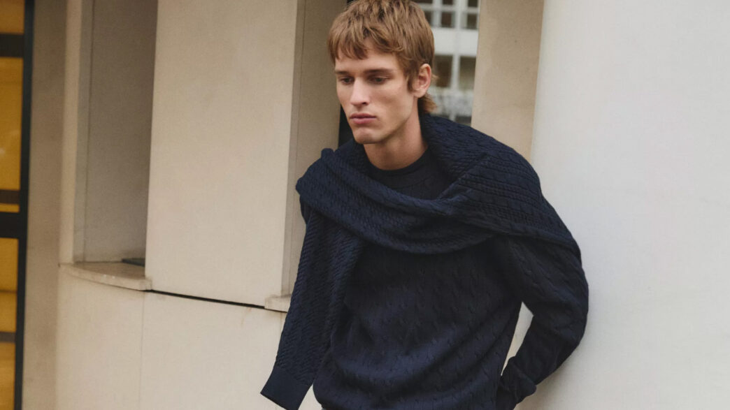 Modelo Jeray Allgayer vestido con un jersey de punto azul marino y otro jersey sobre los hombros.