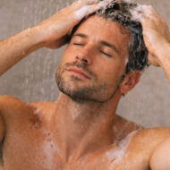 Los mejores champús anticaída para hombre que sí funcionan hombre de 40 años dentro de la ducha masajeándose la cabeza con un champú anticaída
