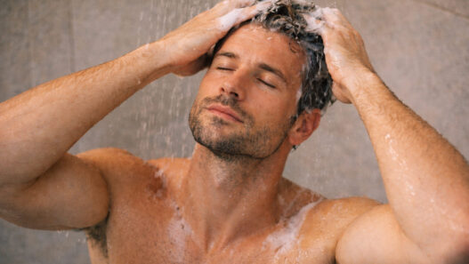 hombre de 40 años dentro de la ducha masajeándose la cabeza con un champú anticaída