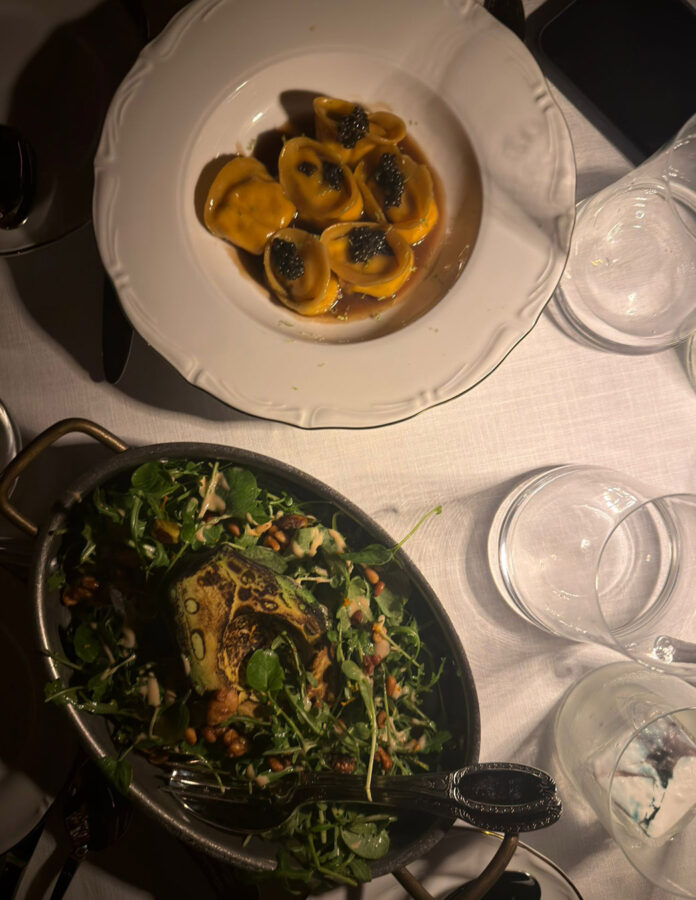 mesa del restaurante 61, con la cena servida: un plato de raviolis y una fuente de verduras. La mesa tiene un mantel blanco muy elegante y copas de cristal