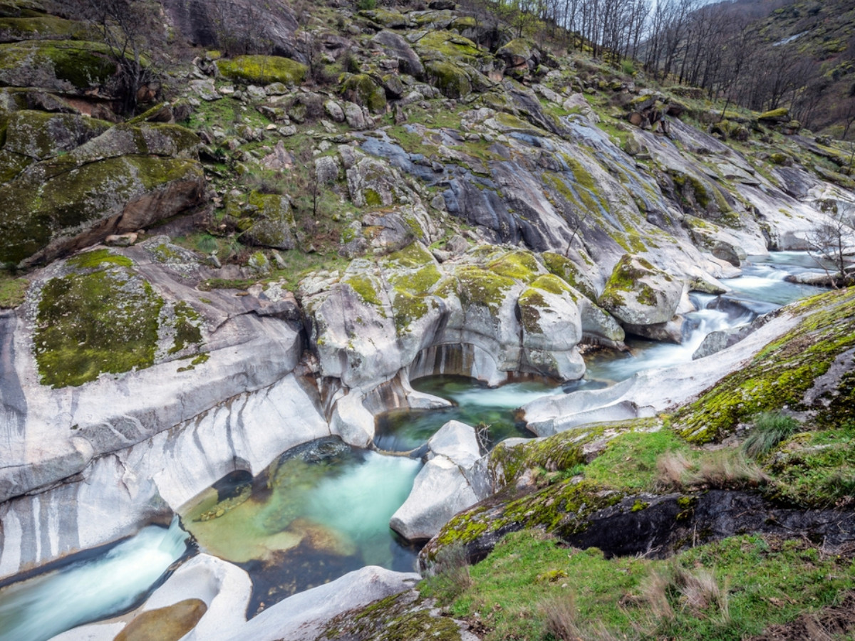 Garganta natural del Valle del Jerte con grandes rocas erosionadas, pozas de agua clara de color turquesa y un arroyo que discurre entre paredes de piedra cubiertas de musgo.