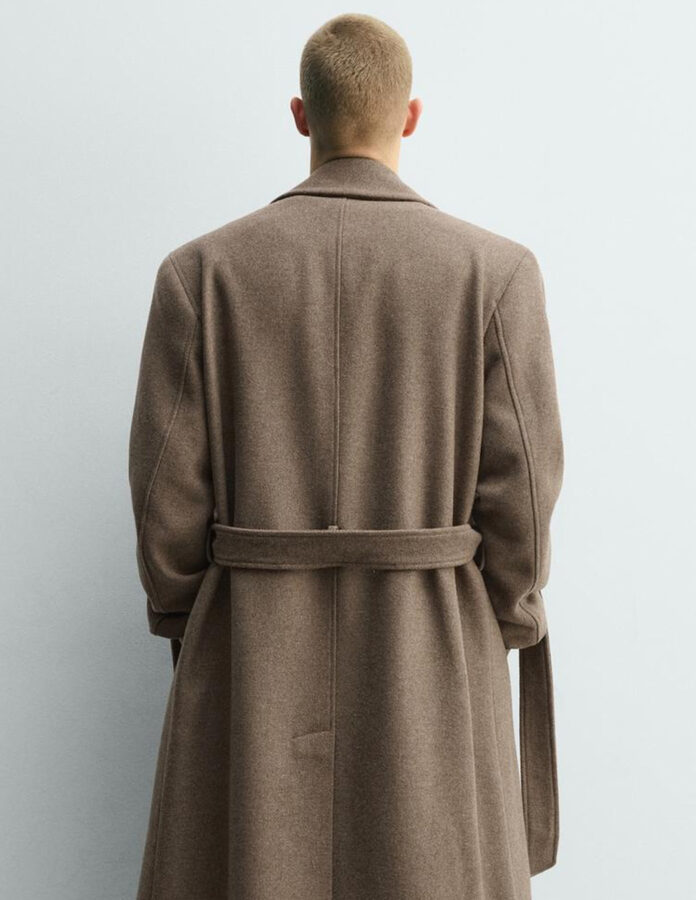 Vista trasera de un abrigo largo camel para hombre, con cinturón del mismo tejido ajustado a la cintura y abertura central en la parte baja de la espalda.