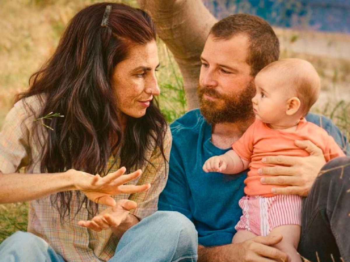 Miriam Garlo con el pelo suelto y una camisa al lado de Álvaro Cervantes con camiseta azul y sujetando a un bebé en una escena de la película Sorda.