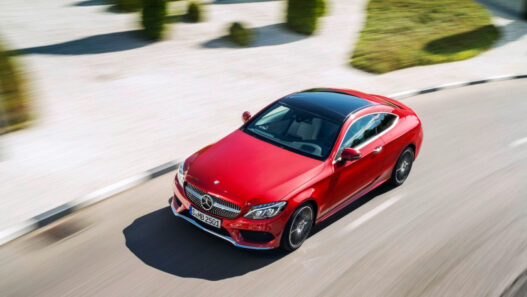 Mercedes-Benz Clase C de color rojo visto desde una perspectiva elevada, circulando por una carretera asfaltada en un entorno despejado y soleado.