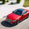 Mercedes-Benz Clase C de color rojo visto desde una perspectiva elevada, circulando por una carretera asfaltada en un entorno despejado y soleado.