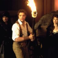Es oficial: La Momia 4 ya tiene fecha de estreno con los protagonistas de la saga original Brendan Fraser con camiseta blanca sujetando una antorcha en la oscuridad junto a Rachel Weisz en La Momia.