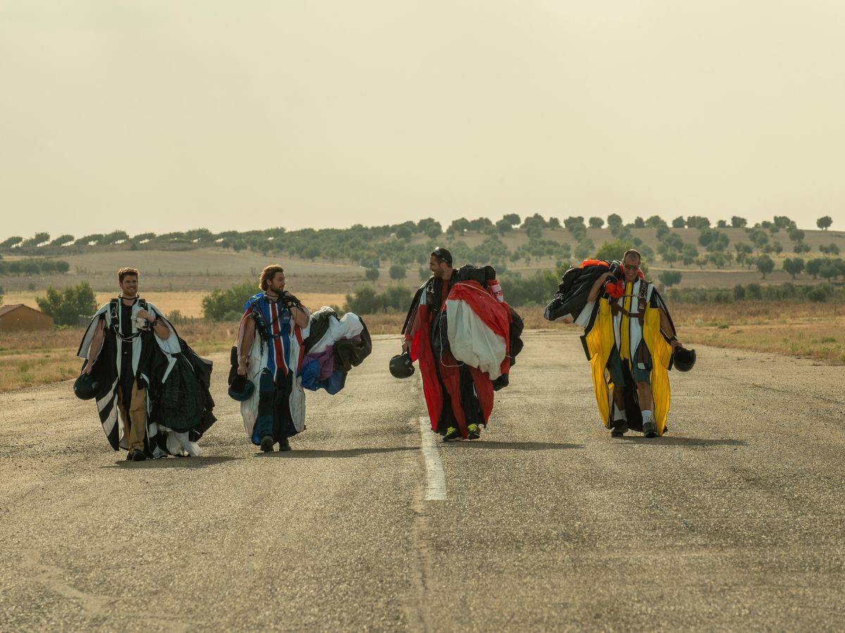 Miguel Ángel Silvestre, Miguel Bernardeau y Carlos Cuevas con trajes de alas en una carretera en una escena de la película La Fiera.