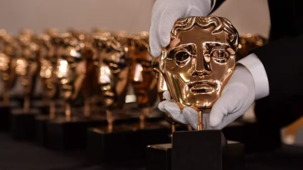 Unas manos con guantes blancos sujetando un Premio BAFTA fabricado en bronce fosforoso.