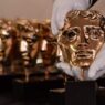 Unas manos con guantes blancos sujetando un Premio BAFTA fabricado en bronce fosforoso.