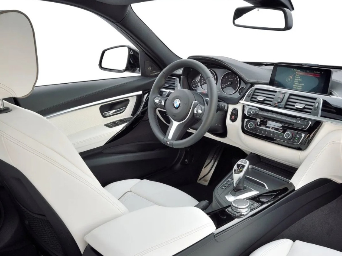 Interior de un BMW Serie 3 visto desde la plaza del acompañante, con volante multifunción, asientos de cuero claros, consola central con mando iDrive y cambio automático.