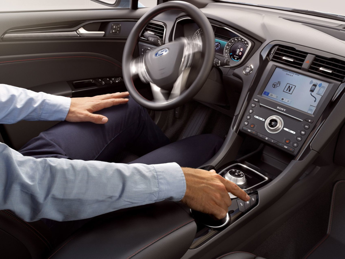 Interior de un Ford Mondeo visto desde el asiento del conductor, con volante multifunción, cuadro de instrumentos analógico y consola central con pantalla y mando giratorio del cambio automático.