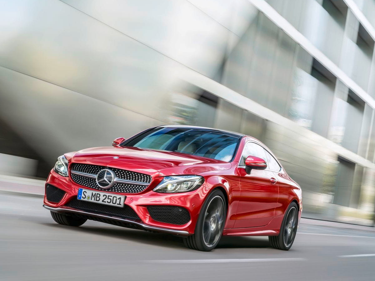 Mercedes-Benz Clase C de color rojo circulando por una vía urbana junto a un edificio moderno, visto desde el frontal izquierdo en movimiento.