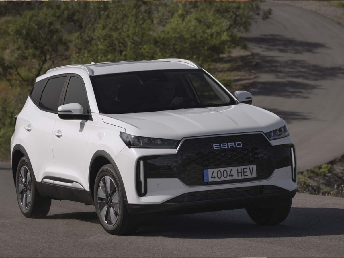SUV compacto EBRO s400 de color blanco circulando por una carretera asfaltada, visto en tres cuartos delanteros, con vegetación y una curva al fondo.