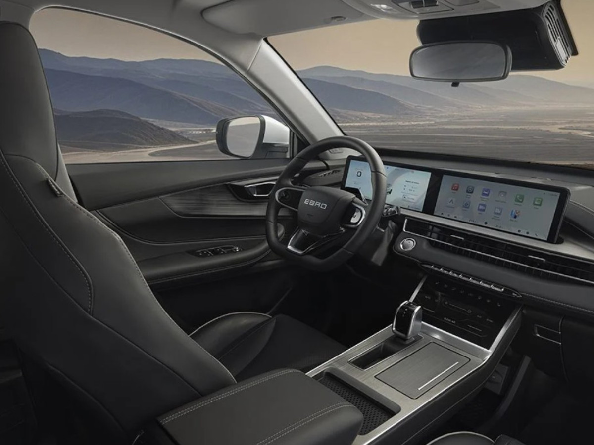 Interior del EBRO s400 con asientos delanteros negros, volante multifunción y salpicadero con doble pantalla digital frente al conductor y la consola central.