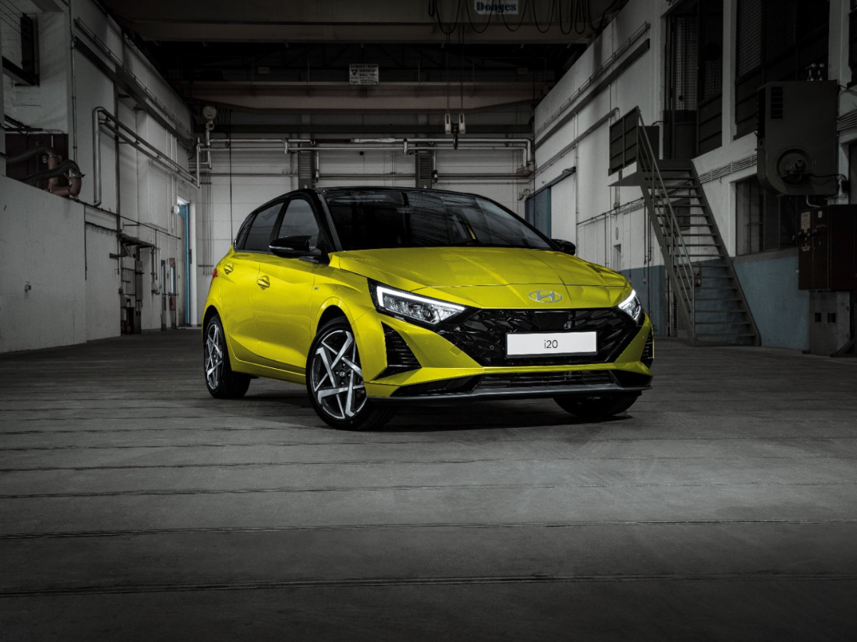 Hyundai i20 de color amarillo aparcado en el interior de una nave industrial, visto en tres cuartos delanteros, con iluminación artificial y fondo metálico.