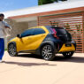 Toyota Aygo X Cross de color amarillo y negro aparcado en el exterior de una vivienda moderna, con una persona caminando junto al coche en un entorno residencial.
