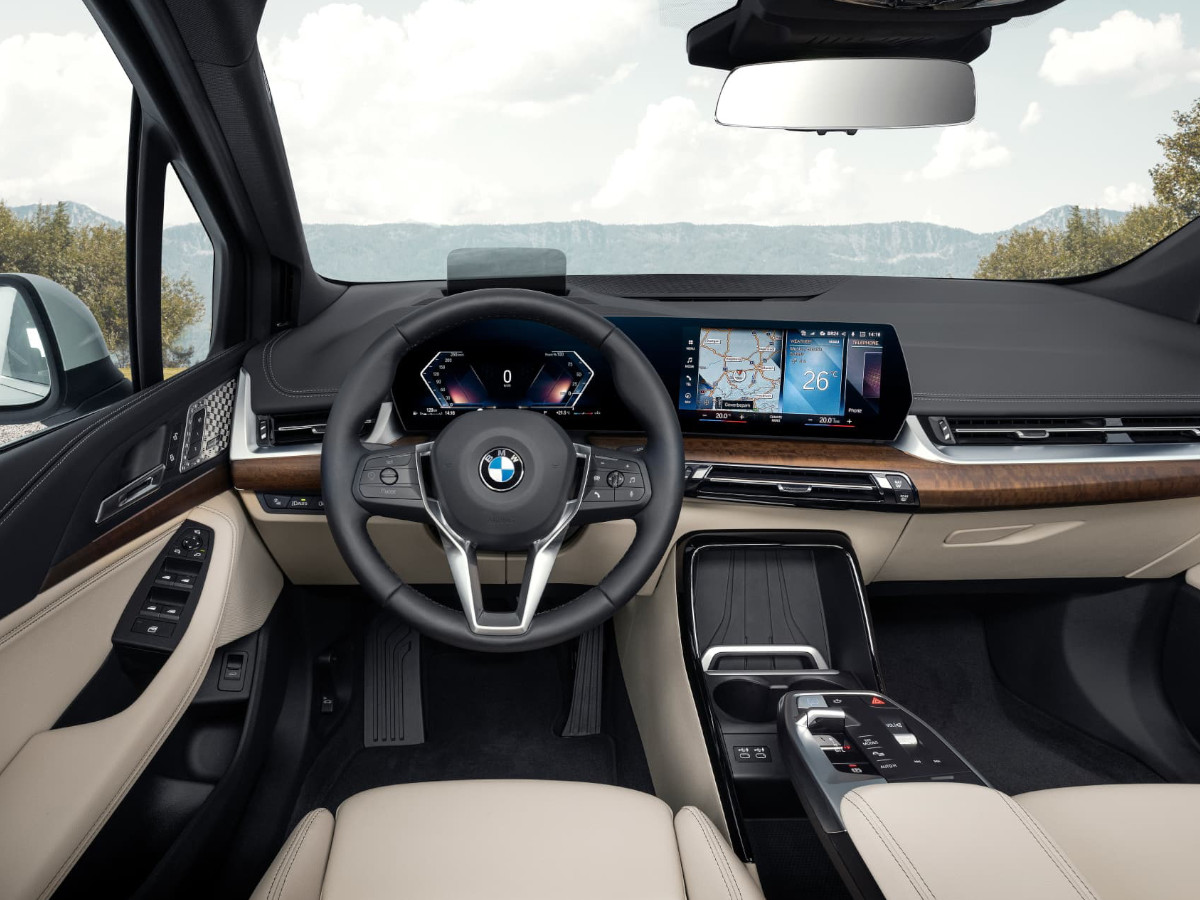 Interior del BMW Serie 2 Active Tourer visto desde el puesto de conducción, con volante BMW, doble pantalla digital y acabados en tonos beige y madera.