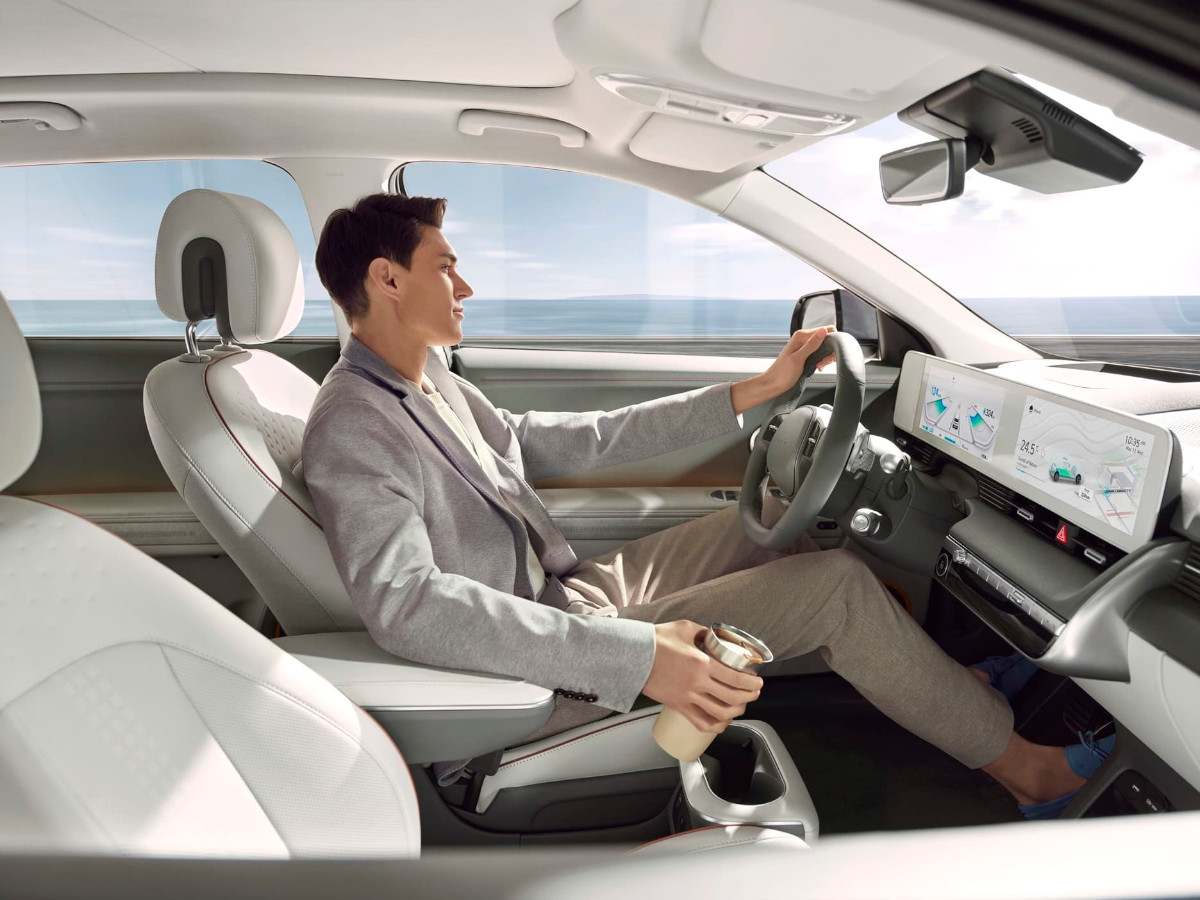 Conductor sentado al volante de un Hyundai Ioniq 5, con interior claro, doble pantalla digital y vista al mar a través del parabrisas durante la conducción.
