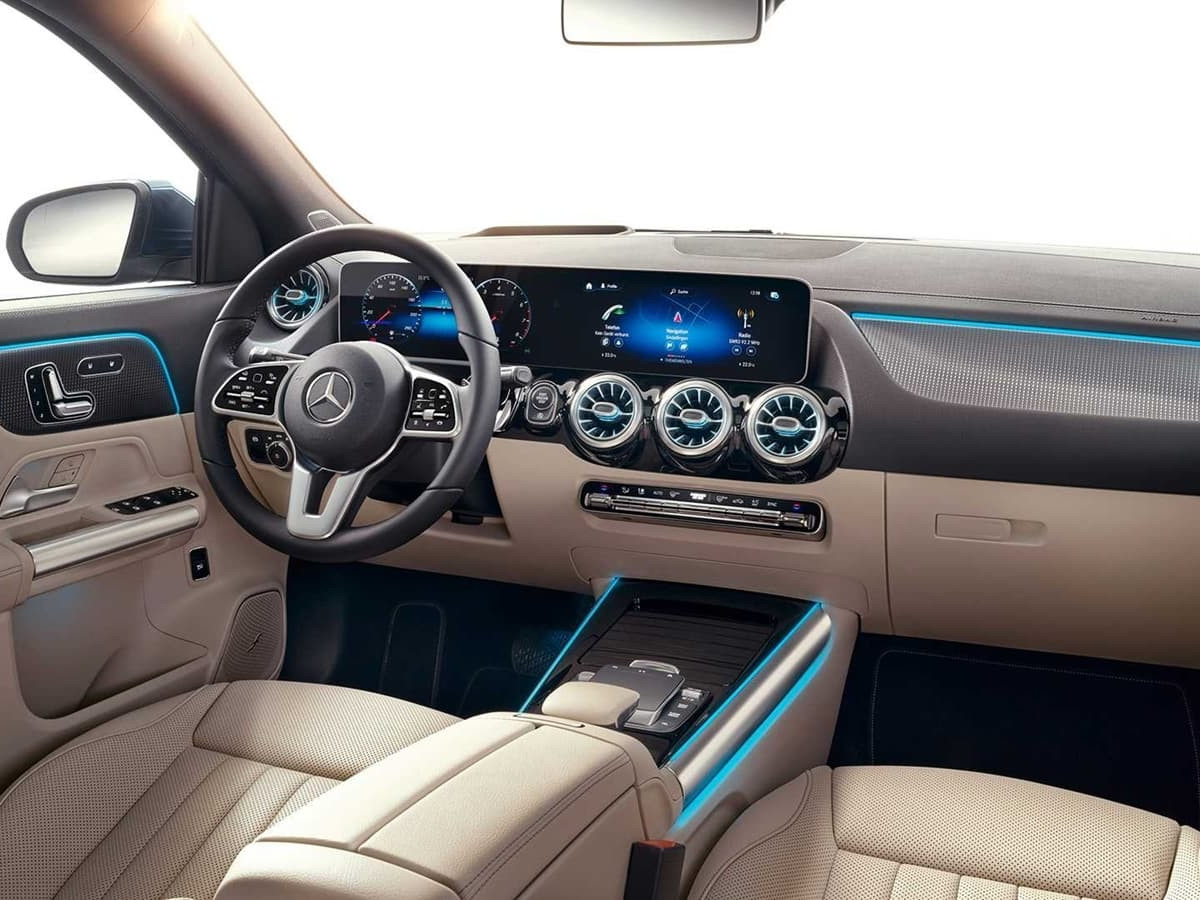 Interior del Mercedes GLA con volante multifunción, doble pantalla panorámica y salpicadero en tonos beige y negros con iluminación ambiental azul.