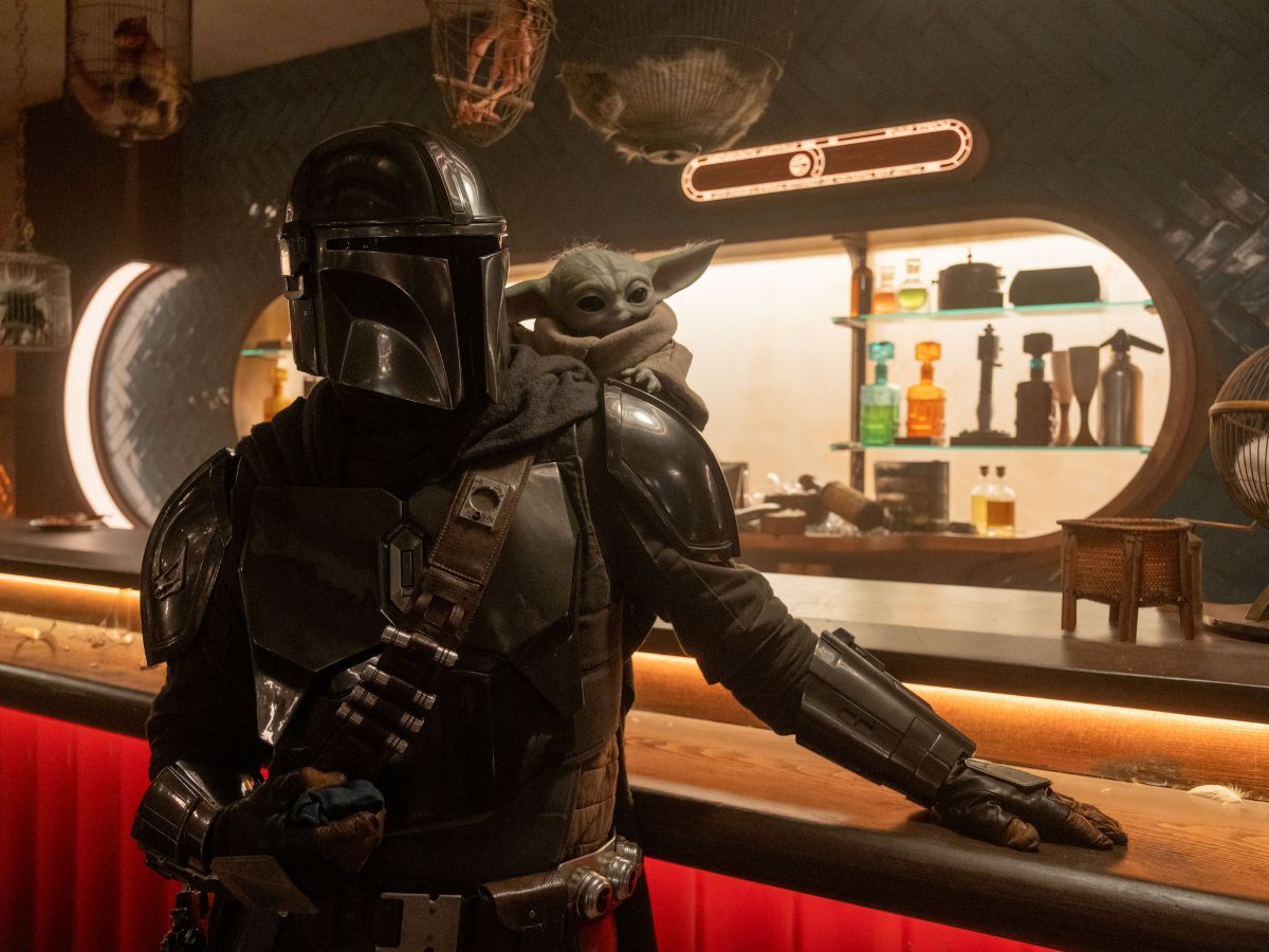 Mando con el traje de cazarrecompensas y en su hombro izquierdo está subido Grogu en una escena en un bar en The Mandalorian and Grogu.