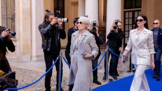 Mery Streep con traje gris en una alfombra azul posando ante los medios y detrás Anne Hathaway en El diablo viste de Prada 2.