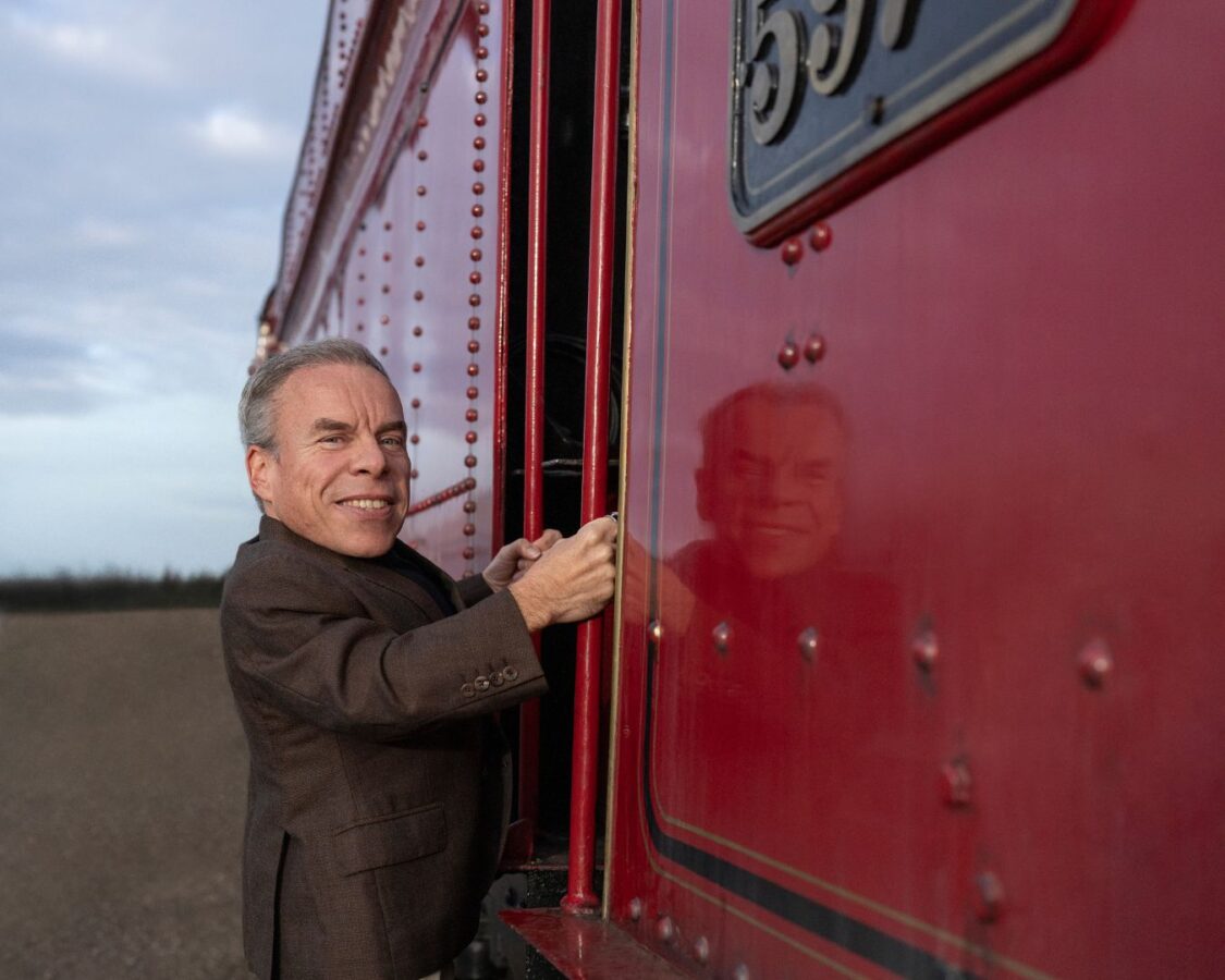 Warwick Davis subido a un tren rojo de Hogwarts como el Profesor Filius Flitwick en la serie de Harry Potter.