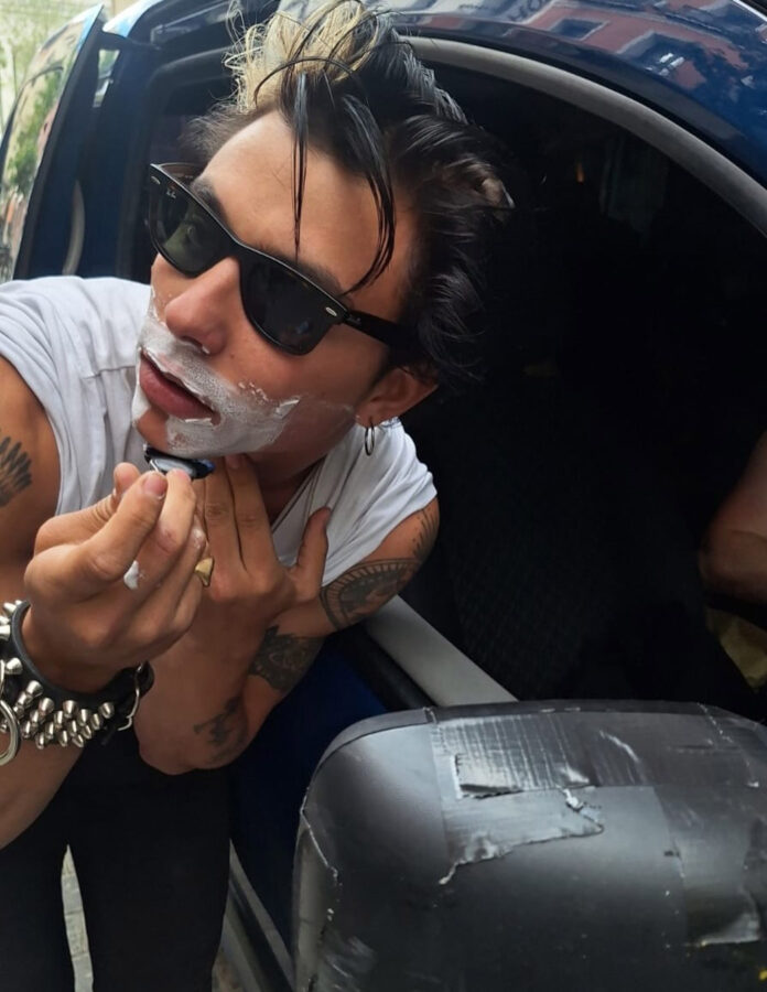 El actor español Mitch afeitándose en el espejo retrovisor de un coche.