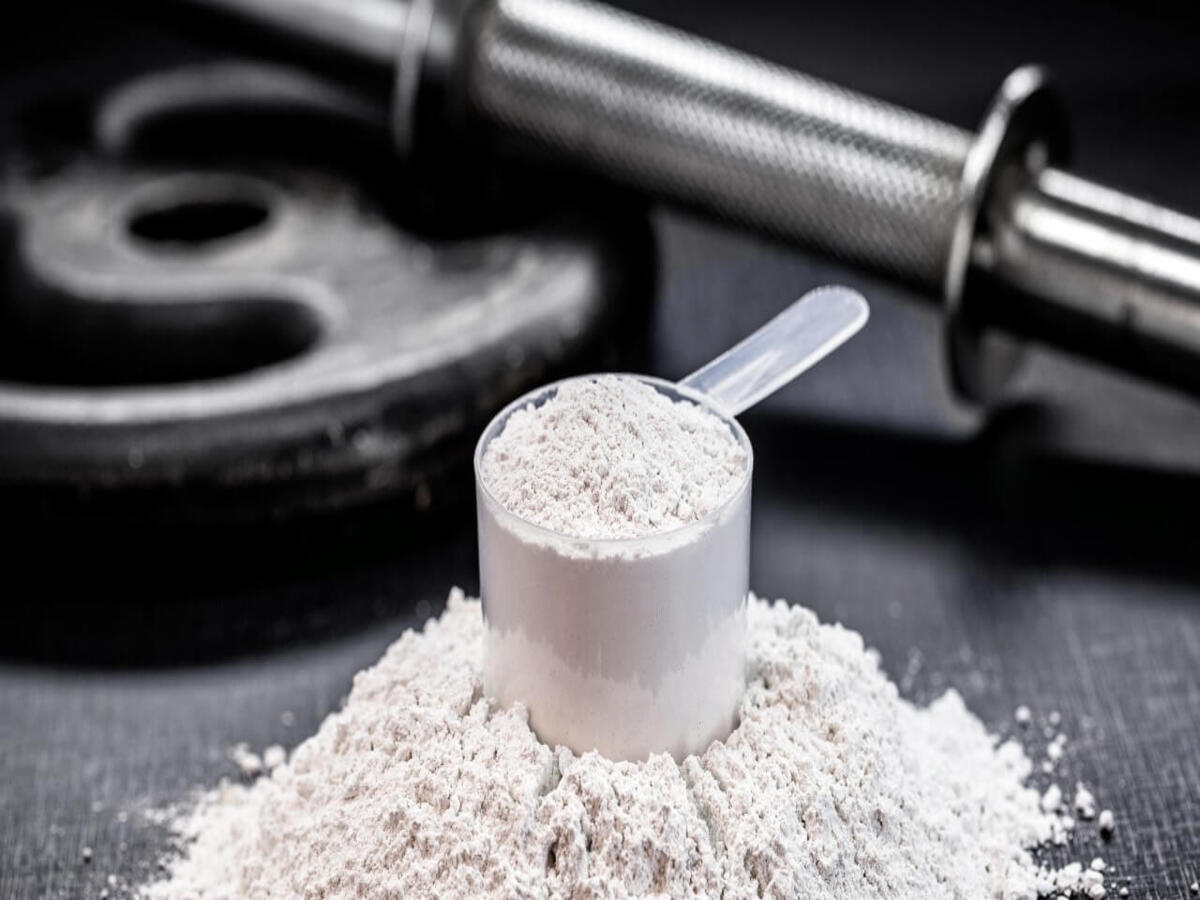 Creatina en polvo junto a pesas, suplemento recomendado para mejorar el rendimiento muscular