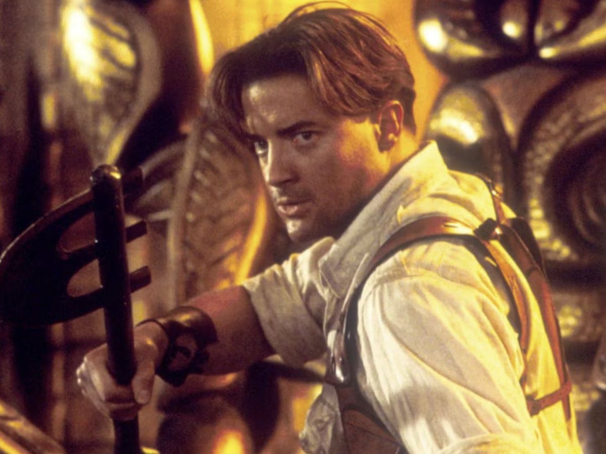 Brendan Fraser con camisa larga blanca y sujetando un arma con la mano derecha en la película La Momia.